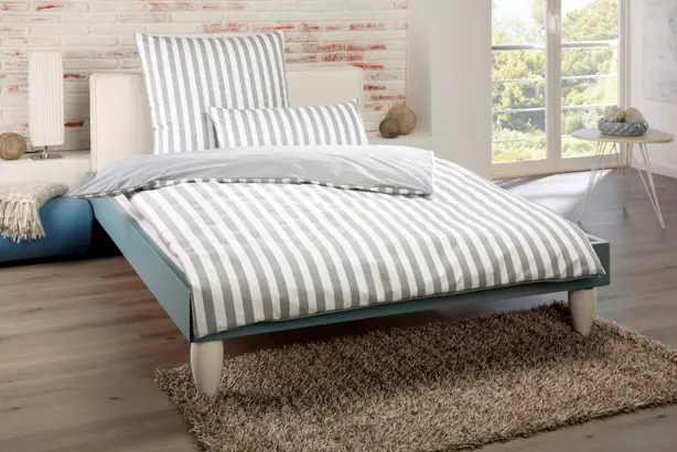 Ein weiß-grau gestreifter Bettbezugbezug der Serie PULMAsoft von MEDI-TECH auf einem türkis-beige farbigen Bett.