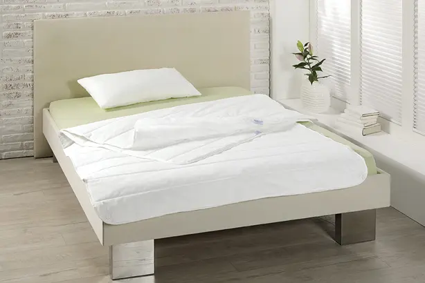 Eine weiße Bettdecke der Serie PULMAsoft von MEDI-TECH auf einem beigen Bett mit hellgrünem Bettlaken.